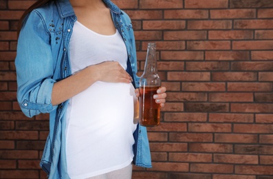 Photo of Future mother with bottle of alcohol drink against brick wall, closeup. Bad habits during pregnancy