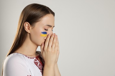Sad young Ukrainian woman with clasped hands on beige background, space for text