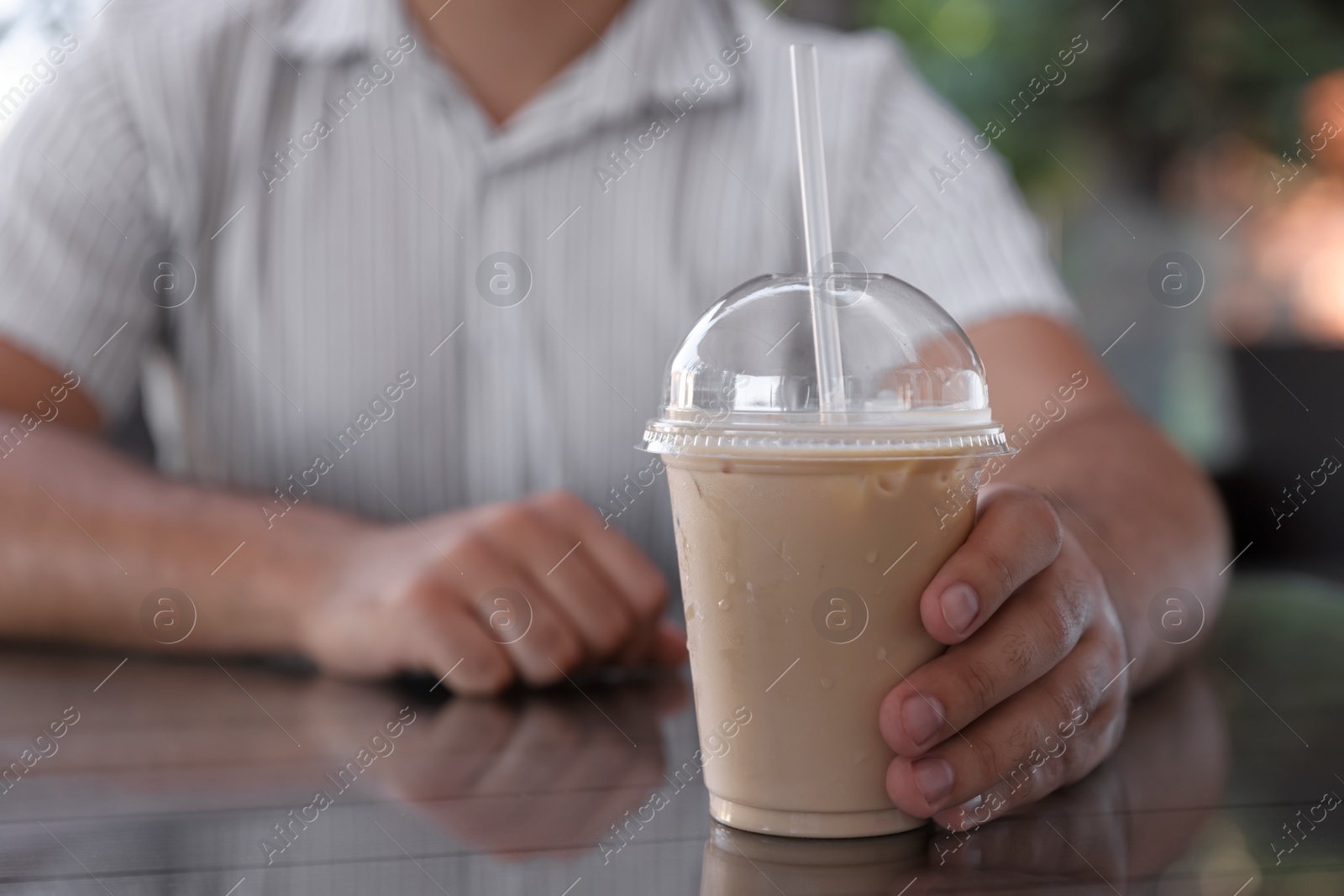 Photo of Man with plastic takeaway cup of delicious iced coffee at table in outdoor cafe, closeup. Space for text