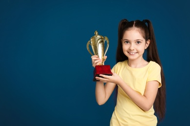 Photo of Happy girl with golden winning cup on dark blue background. Space for text