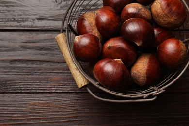 Photo of Sweet fresh edible chestnuts in metal basket on wooden table, top view. Space for text