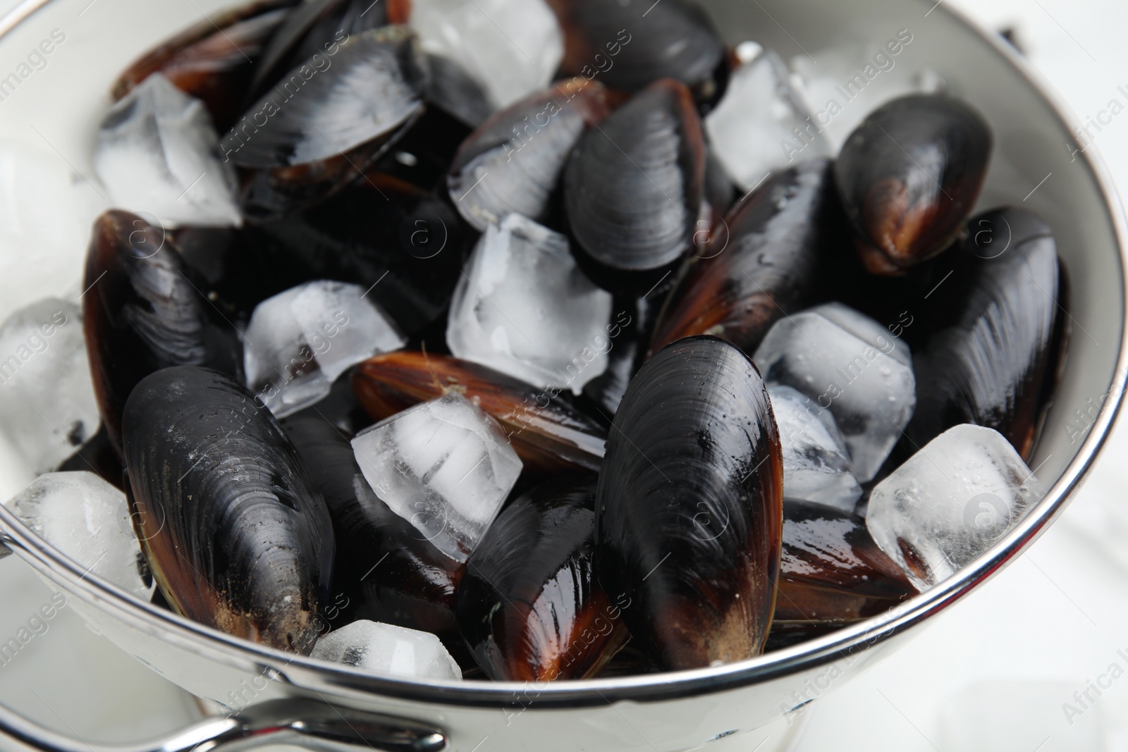 Photo of Colander with raw mussels and ice on white table, closeup