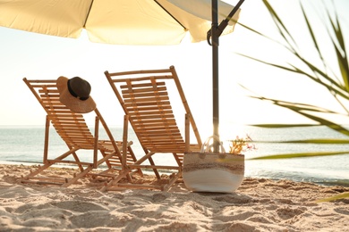 Wooden deck chairs, outdoor umbrella and bag with flowers near sea . Summer vacation