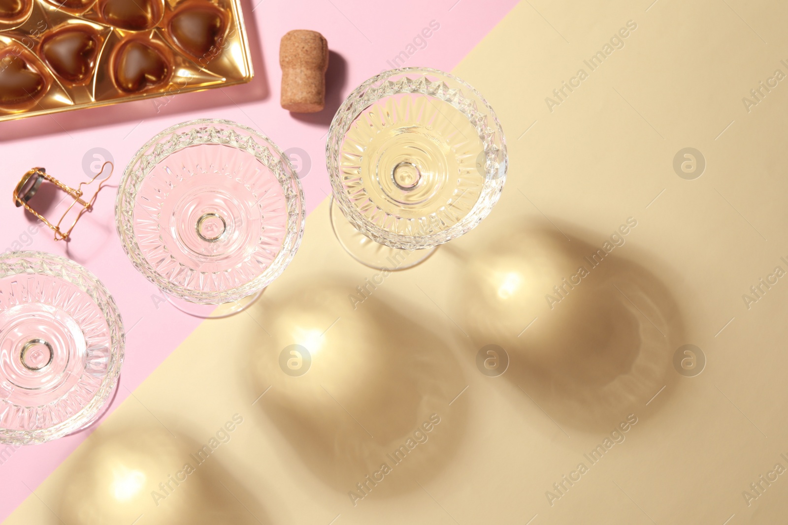 Photo of Glasses of expensive white wine, cork and heart shaped chocolate candies on color background, flat lay. Space for text