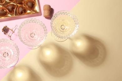Photo of Glasses of expensive white wine, cork and heart shaped chocolate candies on color background, flat lay. Space for text