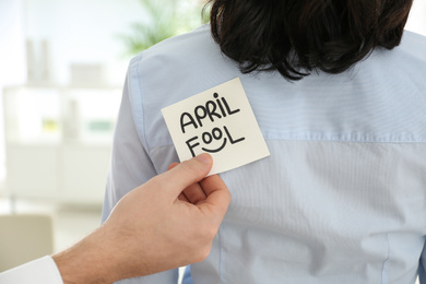 Photo of Man sticking APRIL FOOL note to colleague's back in office, closeup