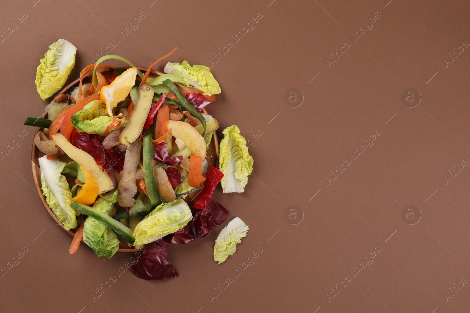 Photo of Peels of fresh vegetables on brown background, top view. Space for text