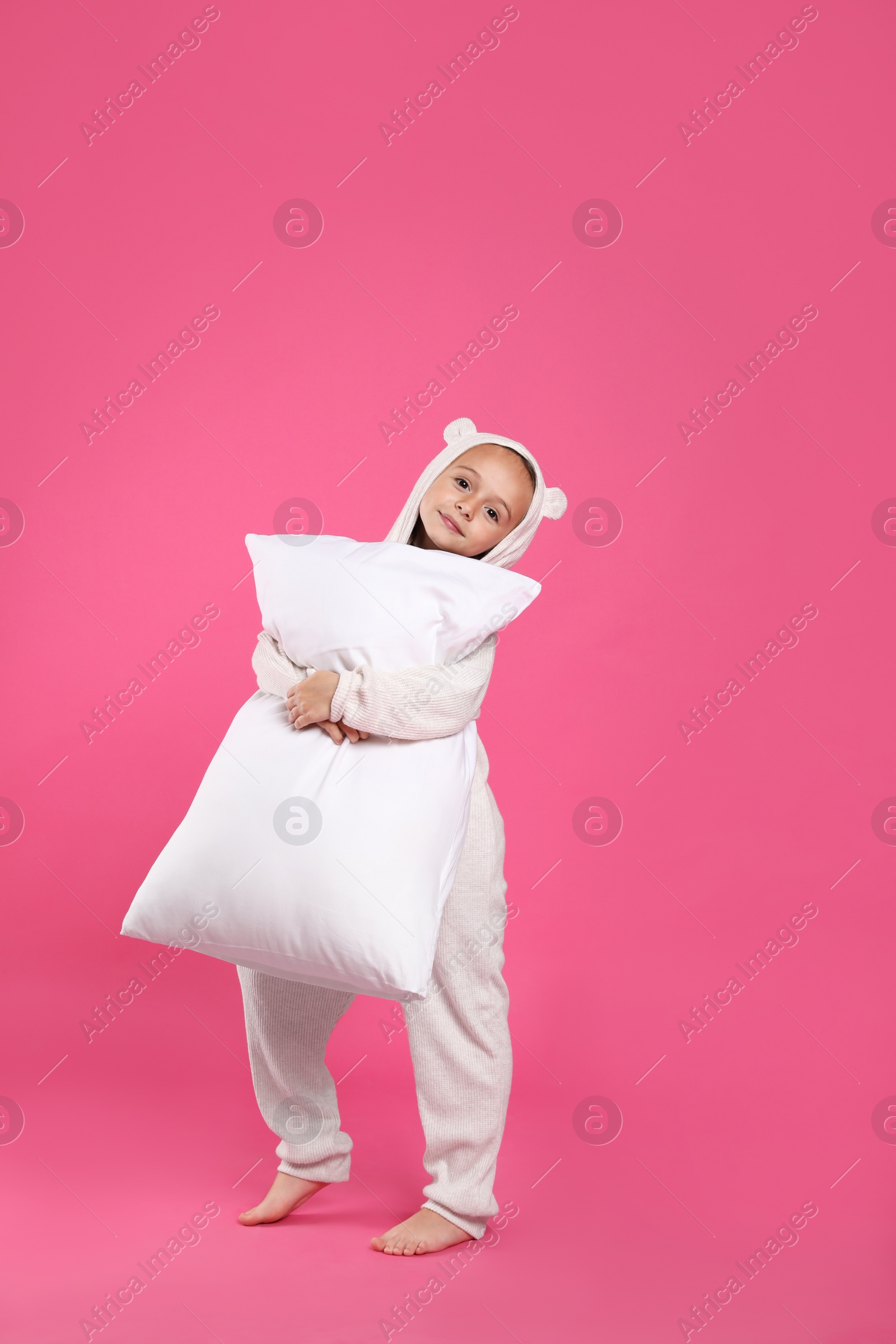 Photo of Cute girl wearing pajamas with pillow on pink background