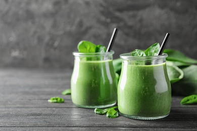 Photo of Jars of healthy green smoothie with fresh spinach on grey wooden table. Space for text