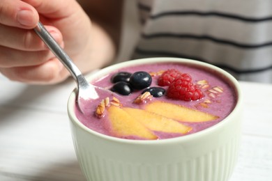 Photo of Woman eating tasty acai smoothie with fruits at white table, closeup