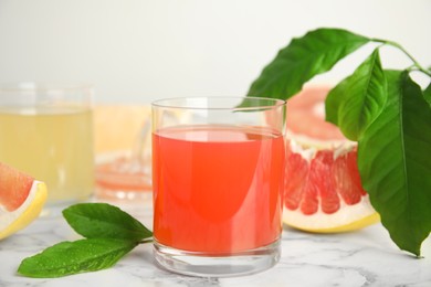 Photo of Glass of pink pomelo juice with green leaves on white marble table