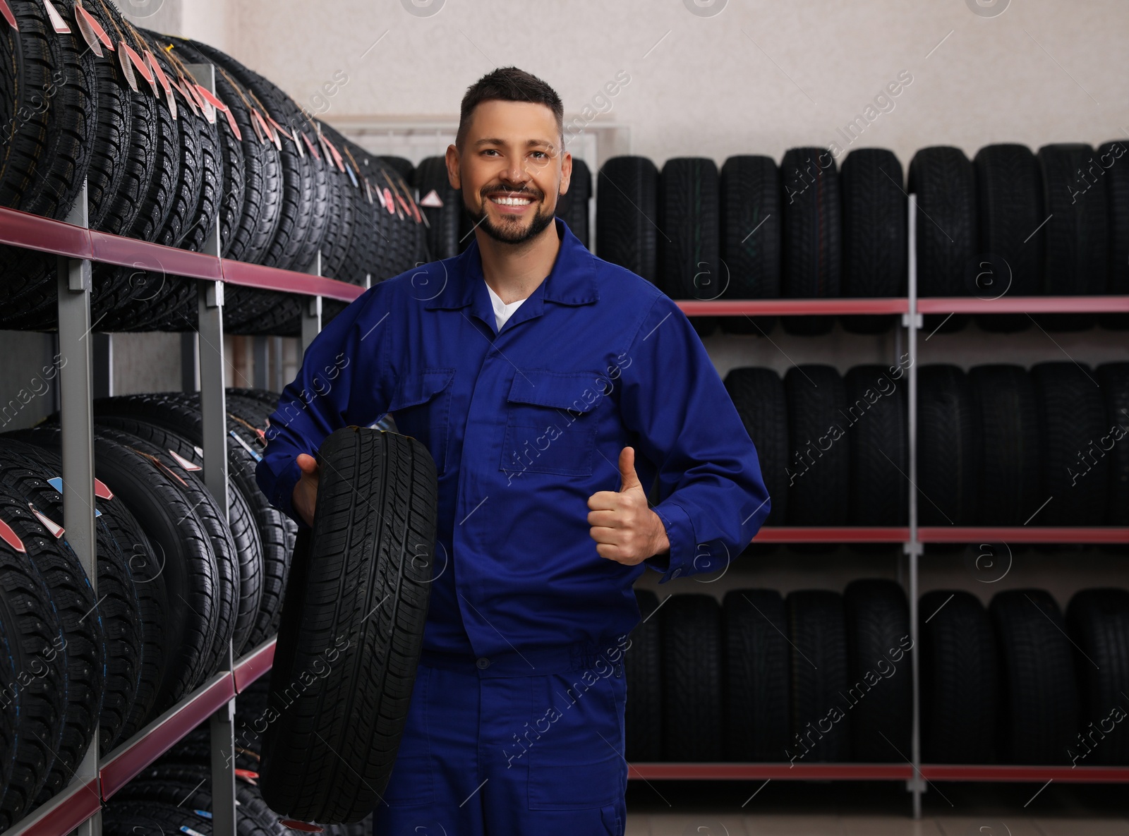 Photo of Male mechanic with car tire in auto store