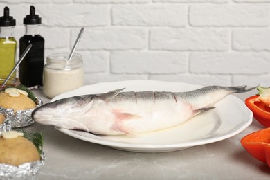 Fresh raw sea bass fish and ingredients on light gray marble table