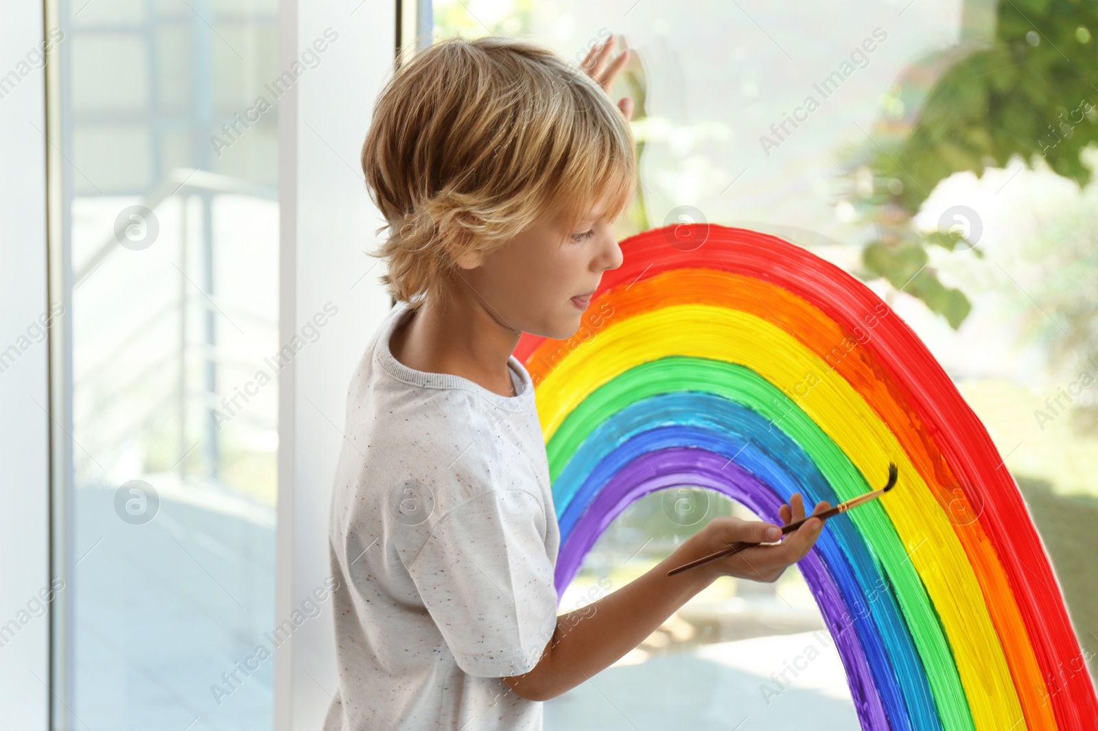 Photo of Little boy drawing rainbow on window. Stay at home concept