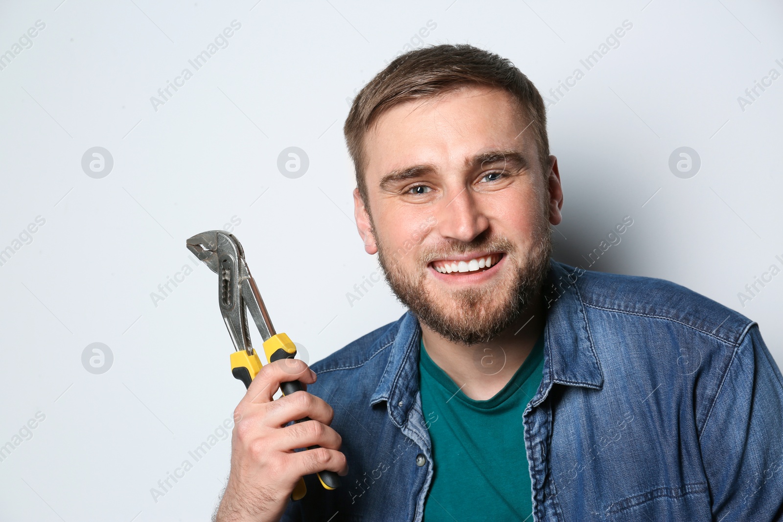 Photo of Young working man with adjustable pliers on light background