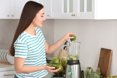 Young woman adding spinach leaves into blender with ingredients for smoothie in kitchen