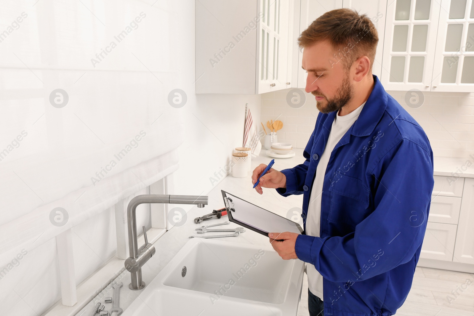 Photo of Plumber with clipboard checking water tap in kitchen