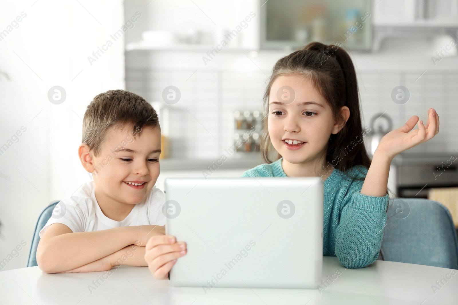 Photo of Little children using video chat on tablet at table in kitchen