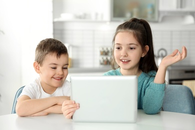 Photo of Little children using video chat on tablet at table in kitchen