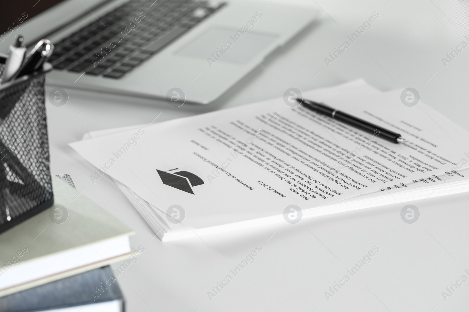 Photo of Acceptance letters from universities with pen and laptop on white table indoors, closeup