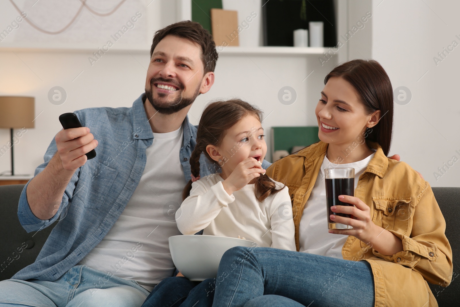 Photo of Happy family watching movie at home. Father changing TV channels with remote control