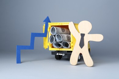 Photo of Economic profit. Wooden figure, arrow and toy truck with banknotes on light grey background