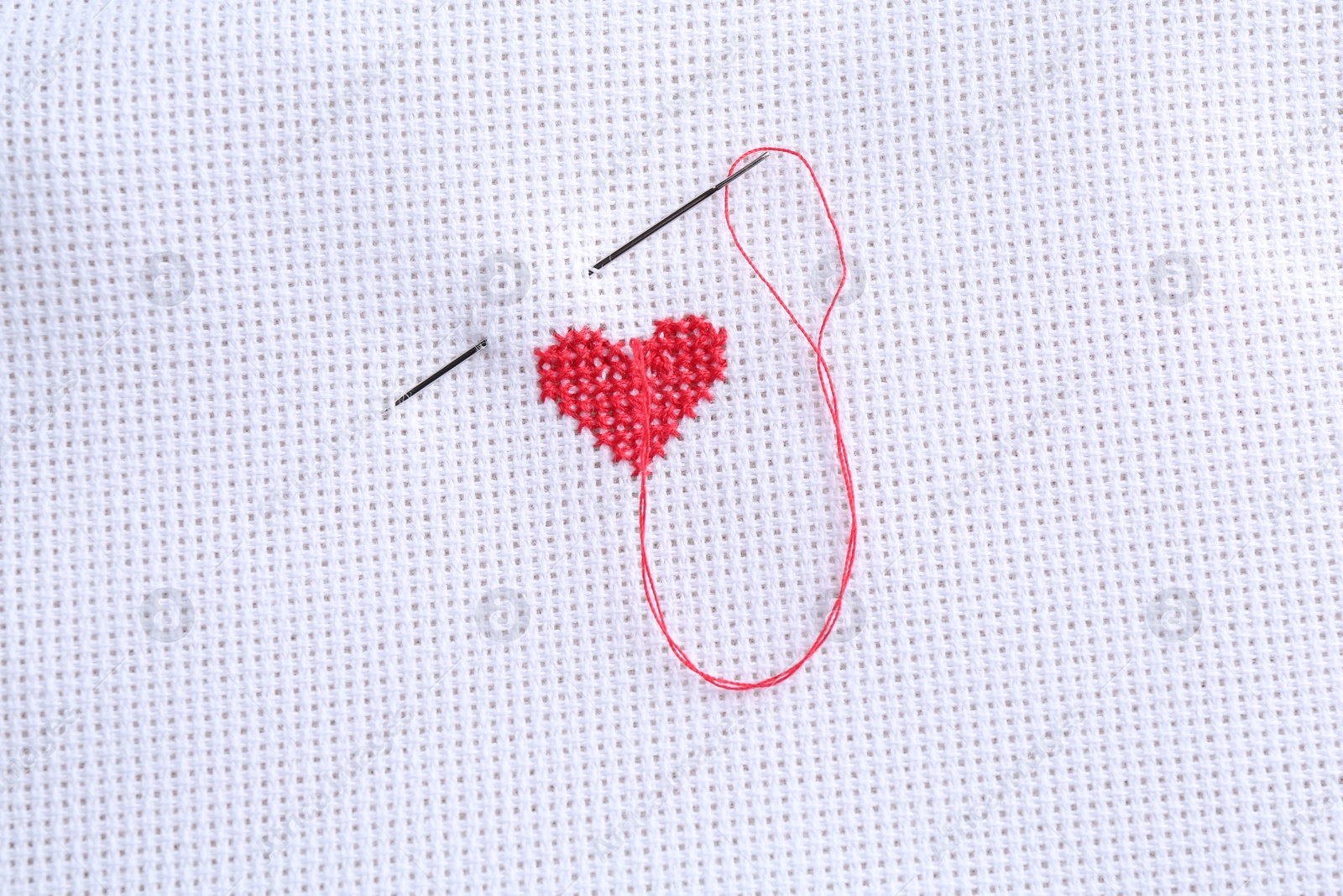 Photo of Embroidered red heart and needle on white cloth, top view