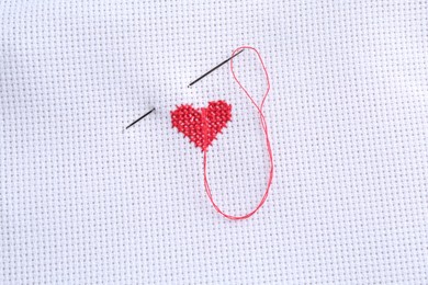 Embroidered red heart and needle on white cloth, top view