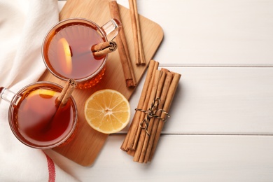 Photo of Delicious hot tea with cinnamon and lemon on white wooden table, flat lay. Space for text