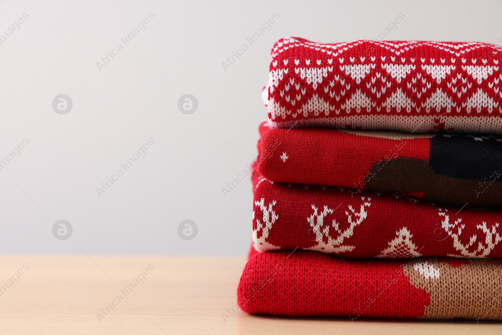 Photo of Stack of different Christmas sweaters on table against light background. Space for text