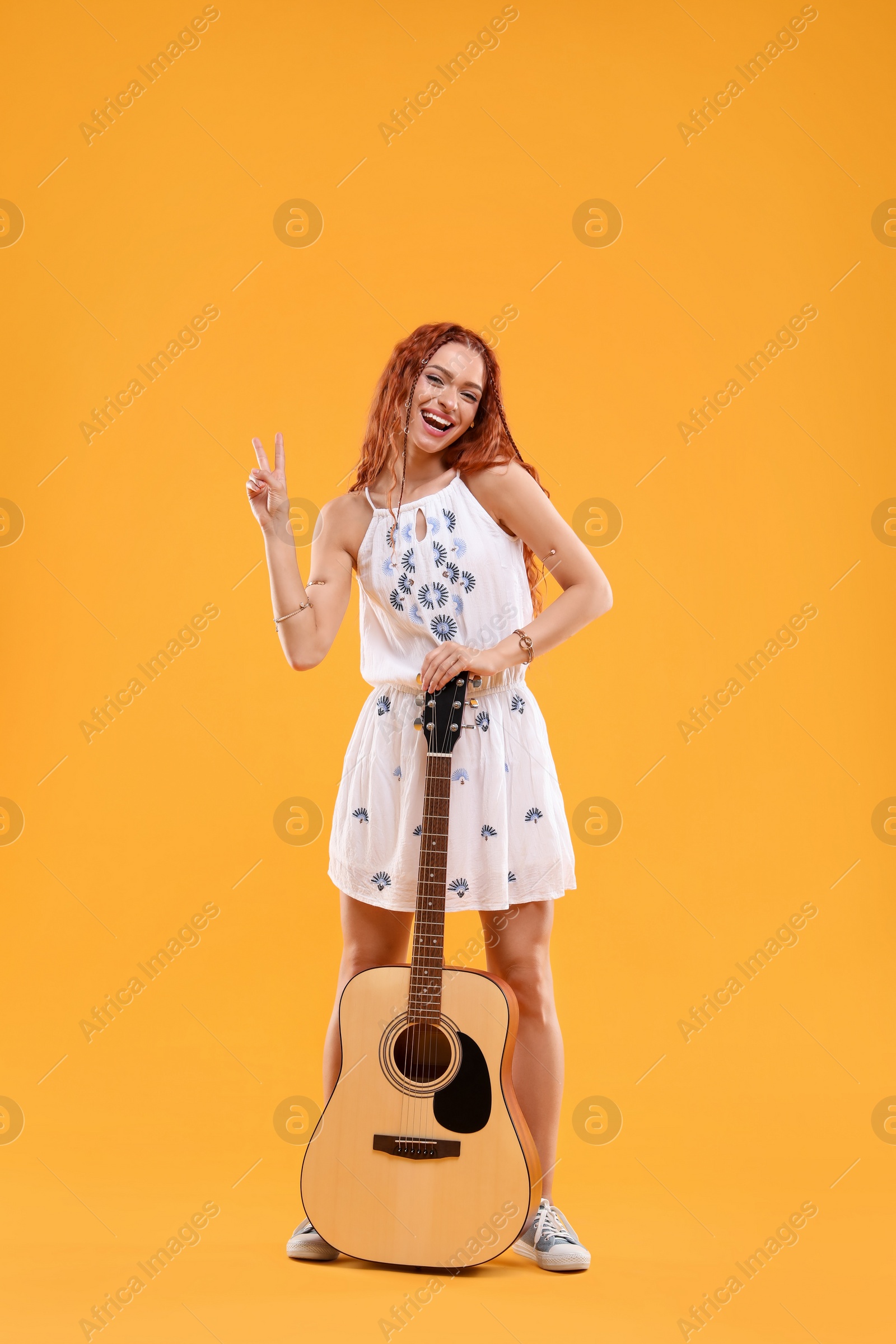 Photo of Beautiful young hippie woman with guitar showing V-sign on orange background