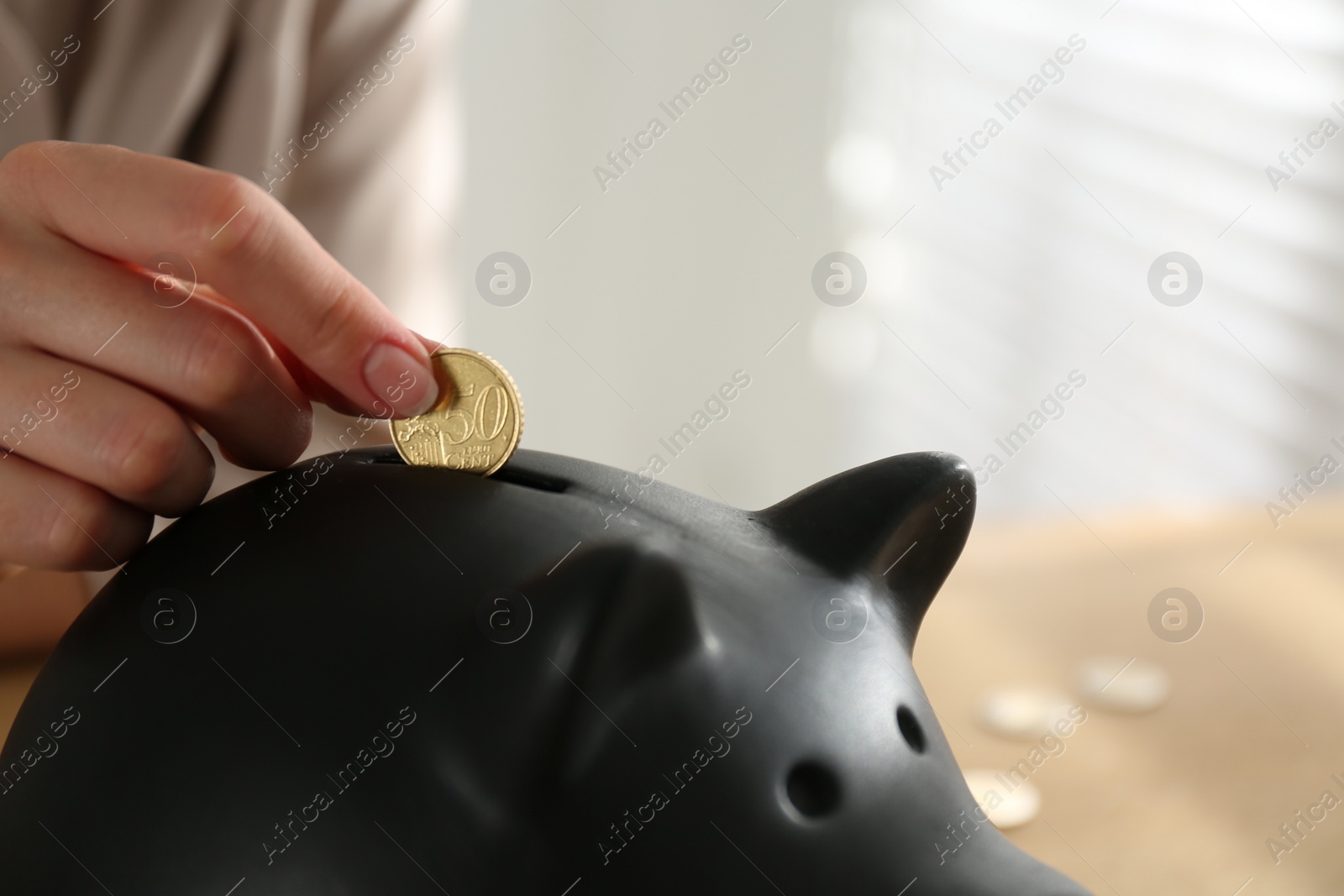 Photo of Woman putting money into piggy bank indoors, closeup