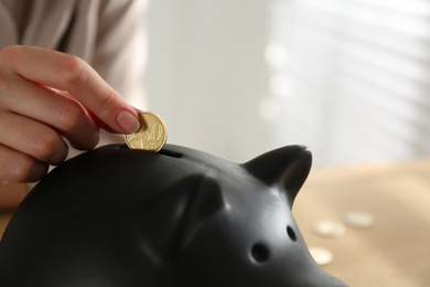 Photo of Woman putting money into piggy bank indoors, closeup