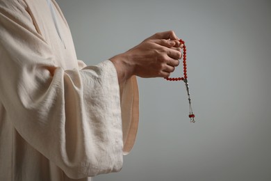 Photo of Muslim man with misbaha praying on light grey background, closeup. Space for text