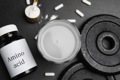 Amino acid shake, powder, pills and weight plates on black background, flat lay