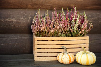 Photo of Beautiful heather flowers in crate and pumpkins on table near wooden wall