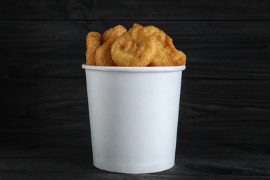 Bucket with tasty chicken nuggets on black table