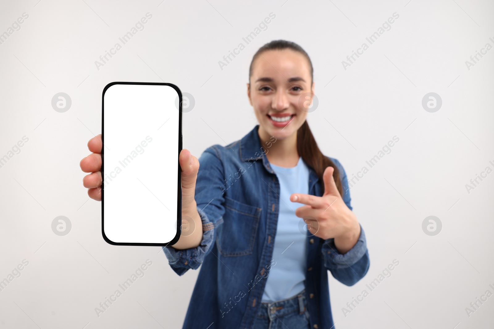 Photo of Young woman showing smartphone in hand and pointing at it on white background, selective focus. Mockup for design