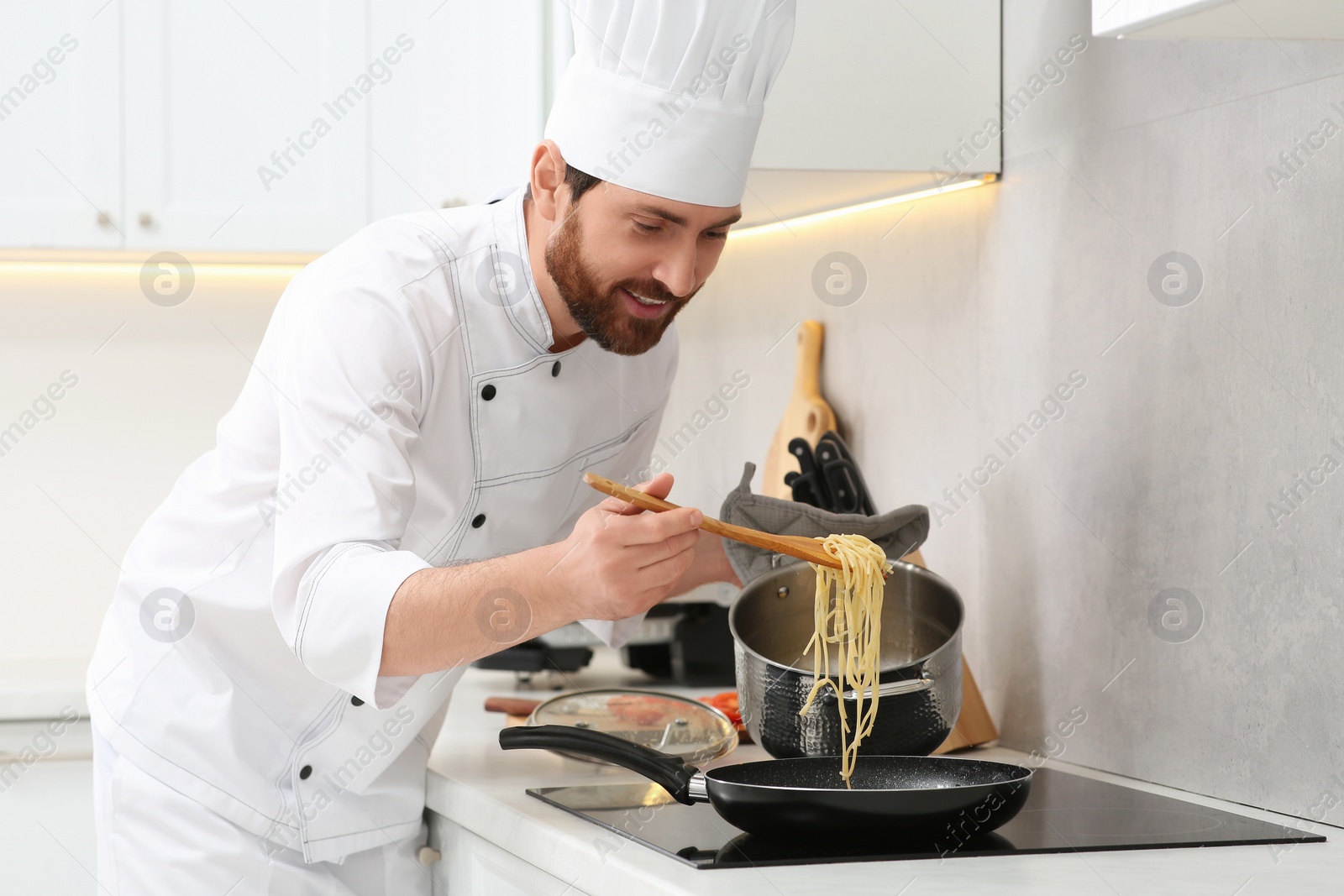 Photo of Chef putting delicious spaghetti from pot into frying pan indoors