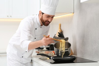 Chef putting delicious spaghetti from pot into frying pan indoors