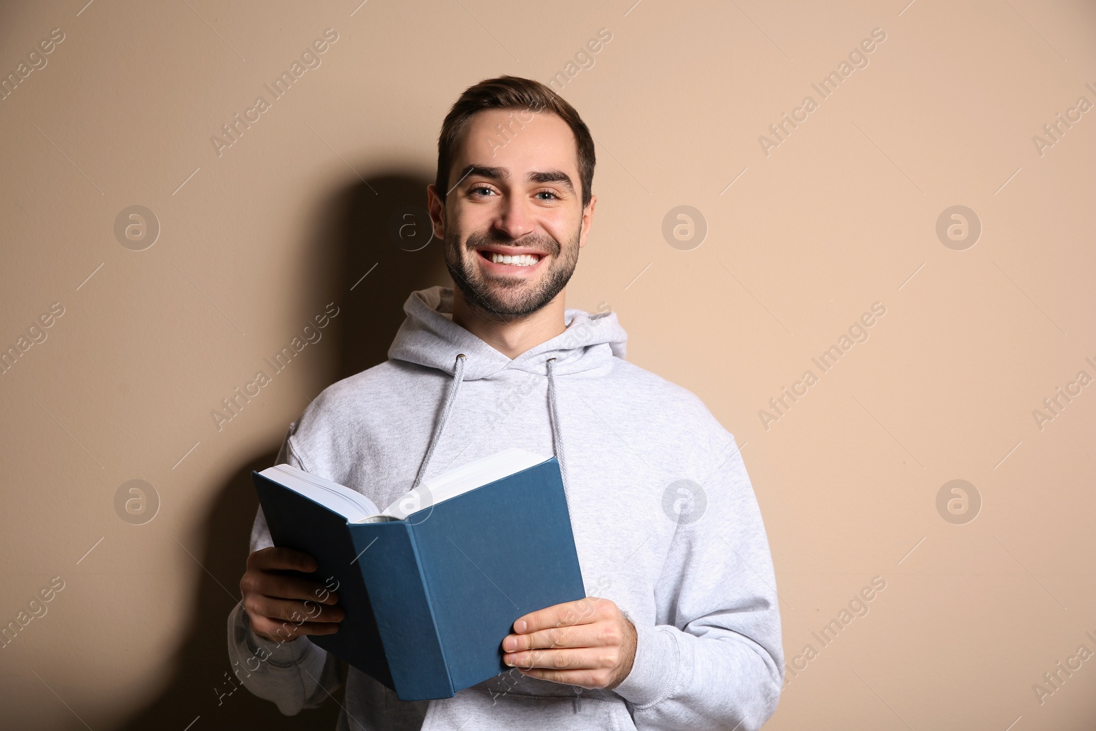 Photo of Young happy man with book on color background