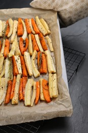 Tray with parchment, baked parsnips and carrots on black table