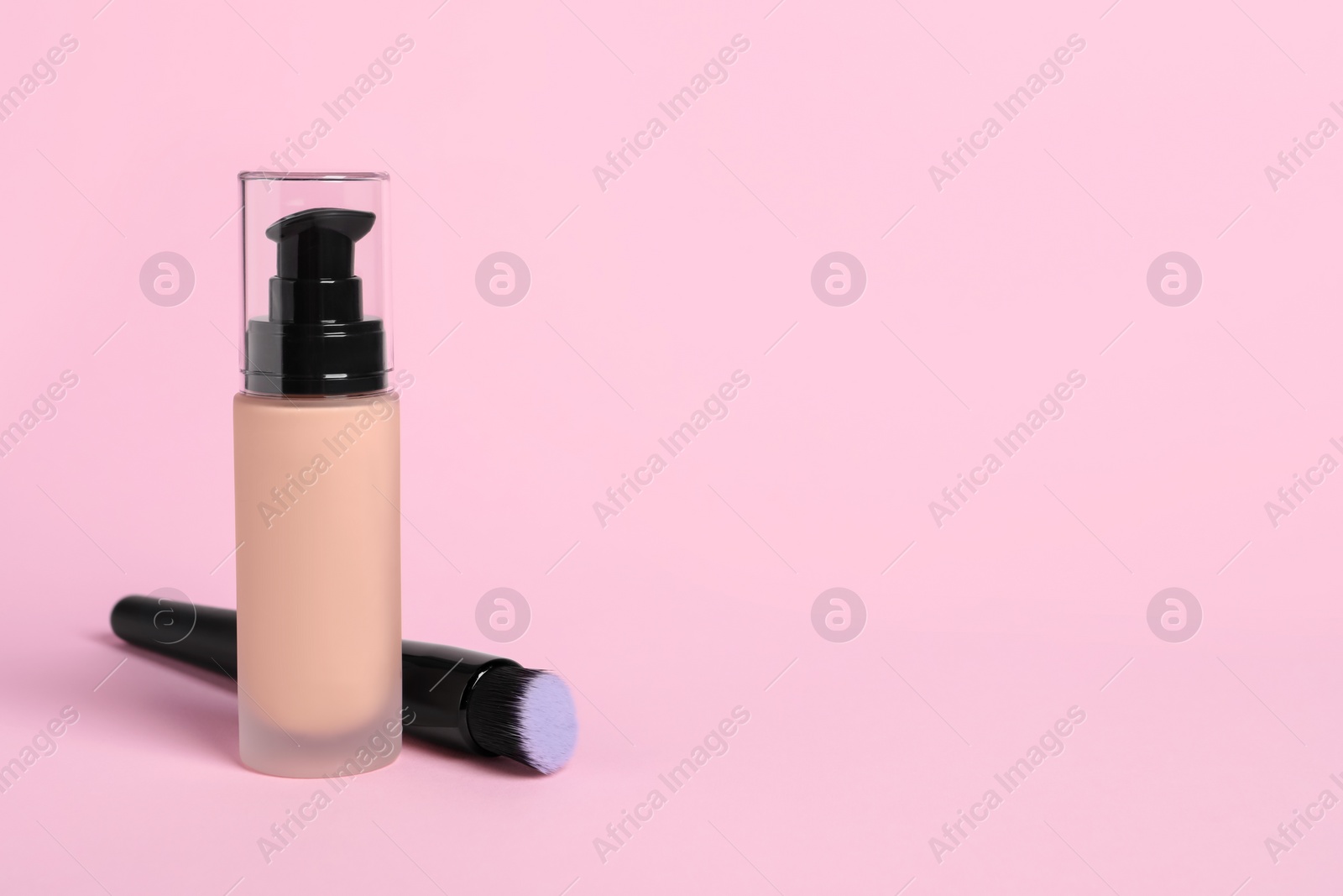 Photo of Bottle of skin foundation and brush on pink background, space for text. Makeup product