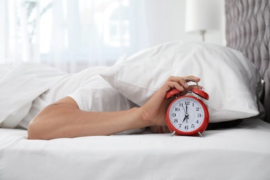 Photo of Man turning off alarm clock in bedroom