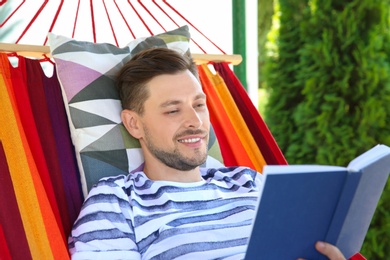 Photo of Man with book relaxing in hammock outdoors on warm summer day
