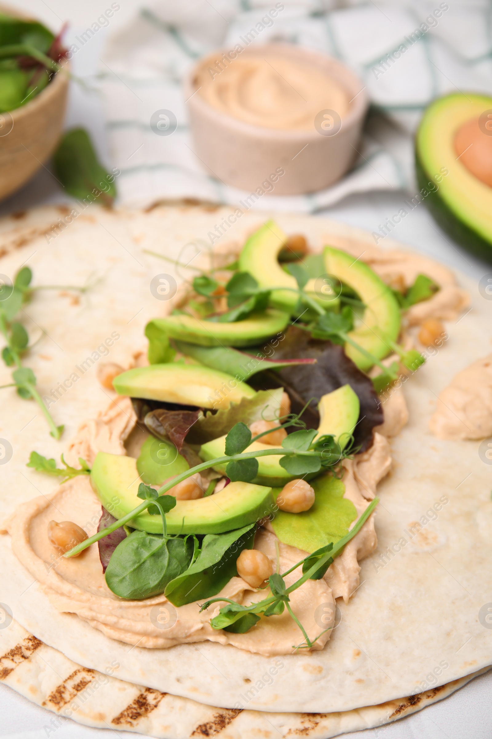 Photo of Tortilla with hummus and vegetables on table, closeup