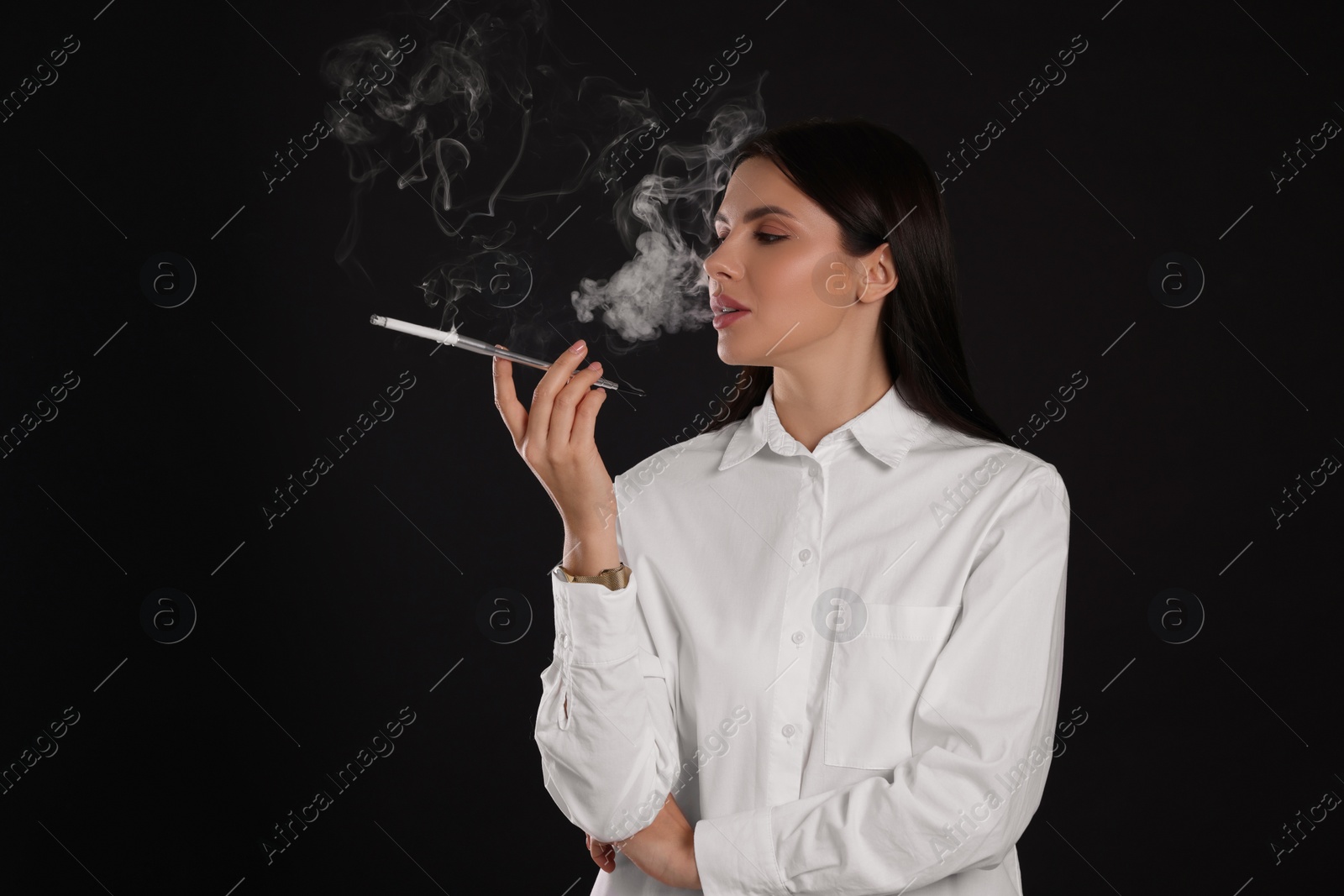 Photo of Woman using long cigarette holder for smoking on black background