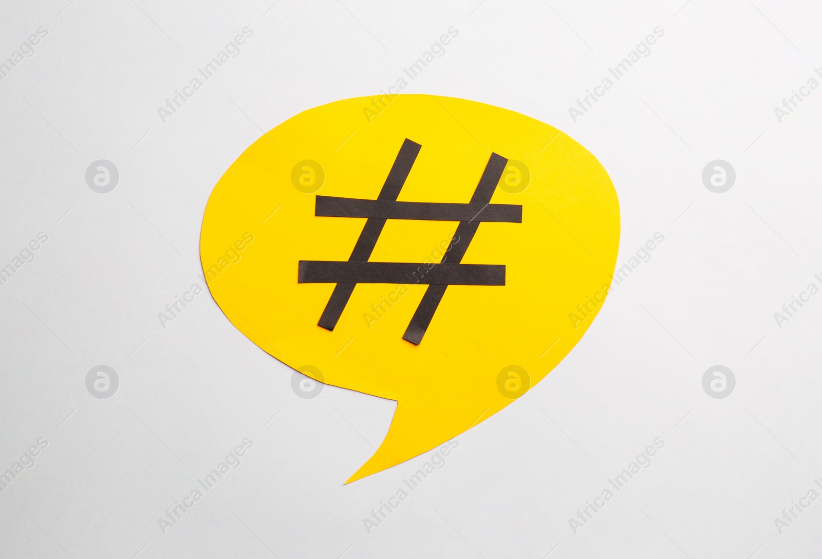 Photo of Yellow paper speech bubble with hashtag symbol on white background, top view