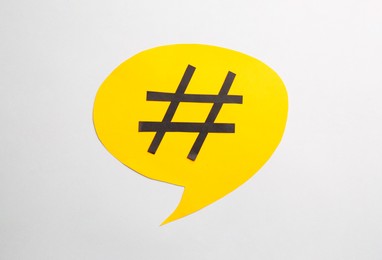 Photo of Yellow paper speech bubble with hashtag symbol on white background, top view