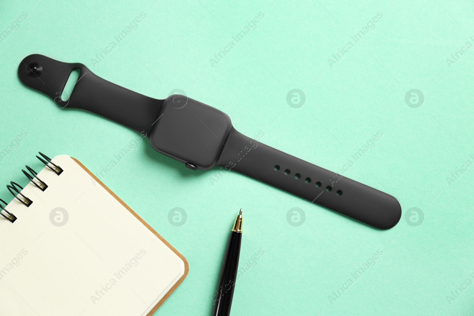 Stylish smart watch, notebook and pen on turquoise background, flat lay Photo of Stylish smart watch, notebook and pen on turquoise background, flat lay